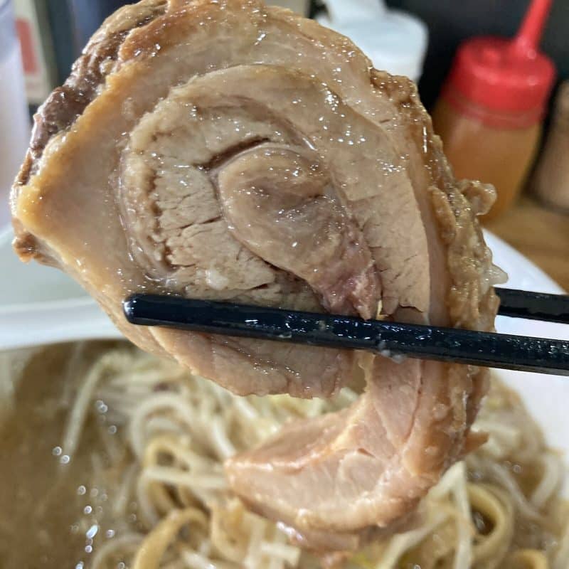 豚レンジャーのラーメン ミニの厚切りチャーシューを箸で持ち上げる