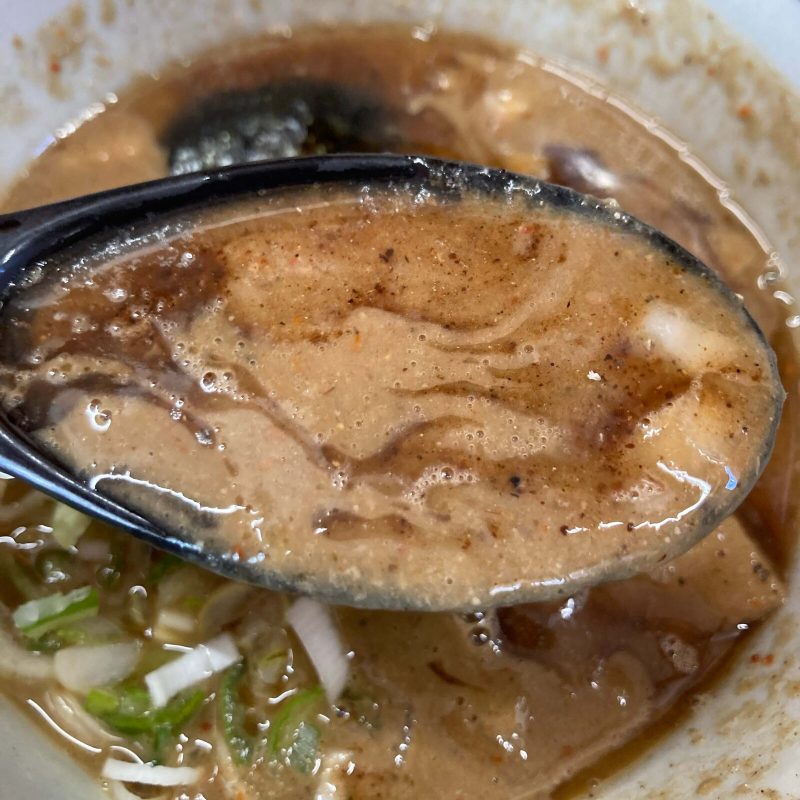 【自家製麺 福は内】のつけ汁を黒いレンゲですくう