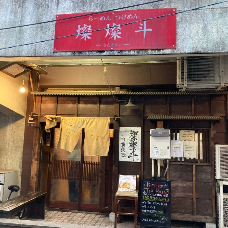 東十条【燦燦斗】の外観 赤い看板と木の引き戸、自家製麺の札